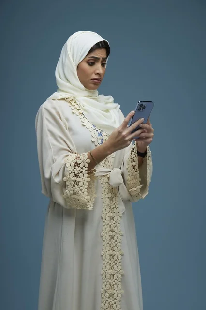 امرأة سعودية بعباءة كريمية تستخدم الهاتف في الاستوديو