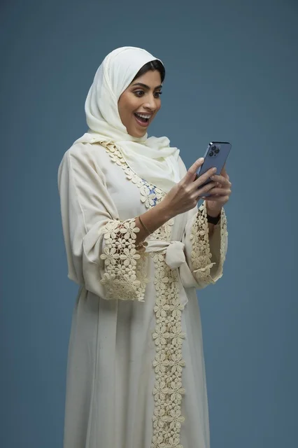 امرأة سعودية بعباءة كريمية تستخدم الهاتف الذكي