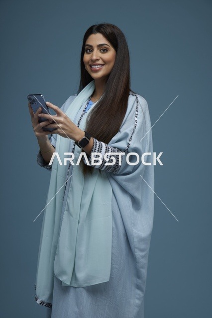 امرأة سعودية مبتسمة تستخدم الهاتف الذكي بخلفية زرقاء