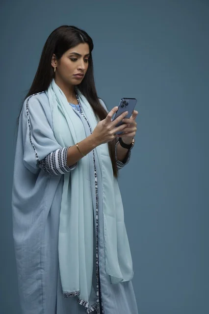 امرأة سعودية تستخدم هاتف ذكي بخلفية زرقاء