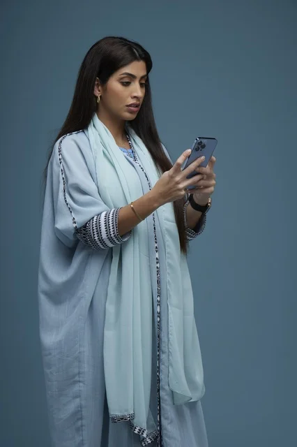 Saudi Woman Using Smartphone on Solid Blue Background