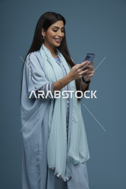 امرأة سعودية مبتسمة تستخدم الهاتف الذكي بعباءة عصرية
