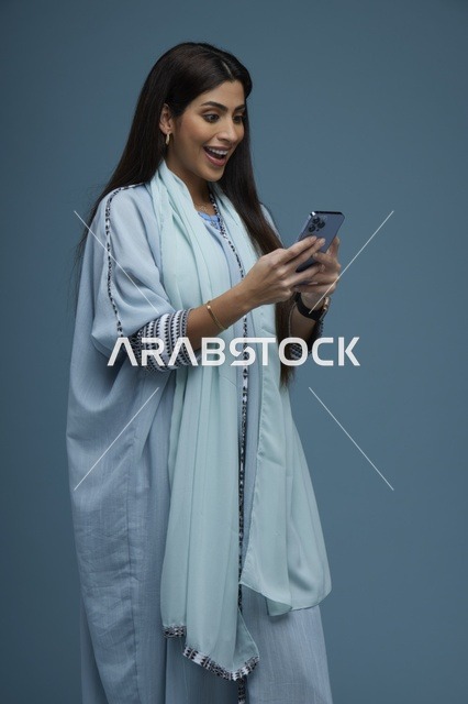 امرأة سعودية مبتسمة تستخدم الهاتف الذكي في الاستوديو