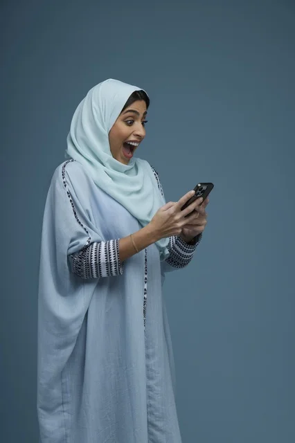 Excited Saudi Woman Using Smartphone on Blue Background