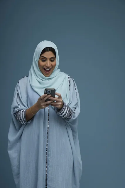 امرأة سعودية متحمسة تنظر إلى شاشة الهاتف الذكي