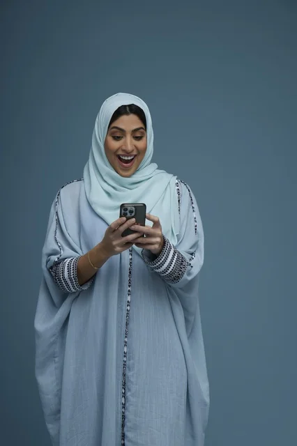 Excited Saudi Woman Using Smartphone on Blue Background