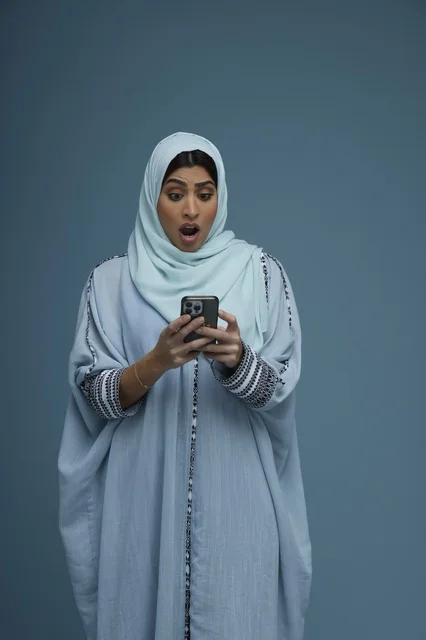 Surprised Saudi Woman Using Smartphone on Blue Background