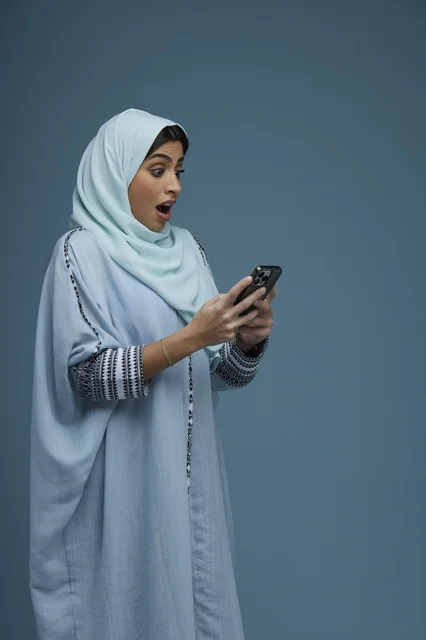 امرأة سعودية مندهشة تتفقد هاتفها الذكي في الاستوديو
