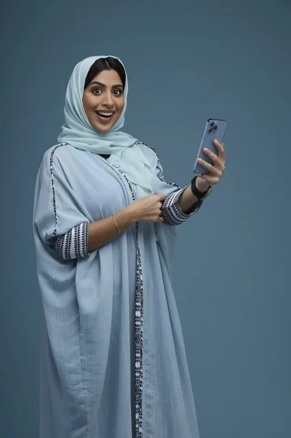 امرأة سعودية متحمسة تشير إلى هاتف ذكي في الاستوديو