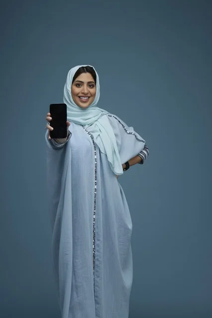 امرأة سعودية مبتسمة تمسك هاتف ذكي في استوديو التصوير