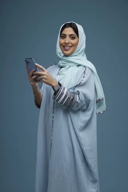 امرأة سعودية مع هاتف ذكي بعباءة زرقاء في الاستوديو