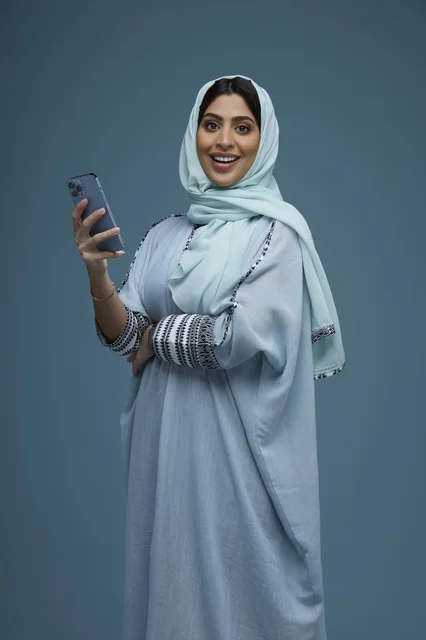 امرأة سعودية تحمل هاتف ذكي بخلفية زرقاء