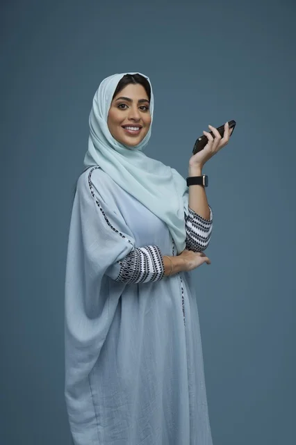 امرأة سعودية تحمل هاتفاً ذكياً أمام خلفية زرقاء