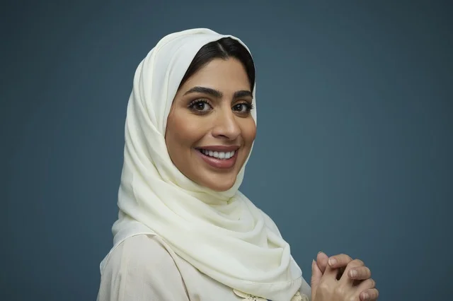 امرأة سعودية بالحجاب الأبيض تبتسم في لقطة بورتريه