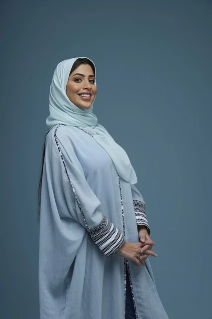بورتريه امرأة سعودية بعباءة زرقاء تبتسم في استوديو