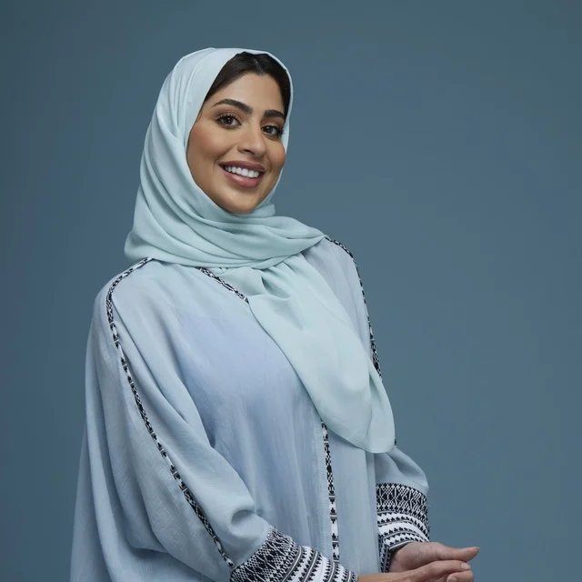 امرأة سعودية محجبة مبتسمة أمام خلفية استوديو زرقاء