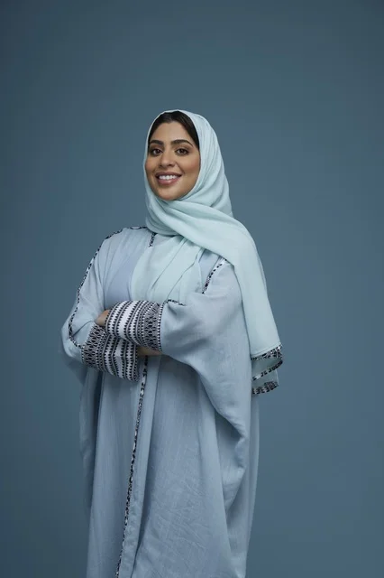 امرأة سعودية مبتسمة بعباءة زرقاء في الاستوديو