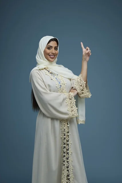 Smiling Saudi Woman in White Abaya Pointing Up in Studio