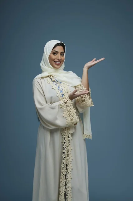 امرأة سعودية بعباءة بيضاء تشير بيديها في الاستوديو