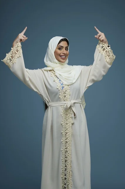 Smiling Saudi Woman in White Abaya Pointing Upwards
