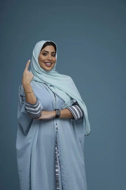 امرأة سعودية تشير للأعلى بعباءة زرقاء في الاستوديو