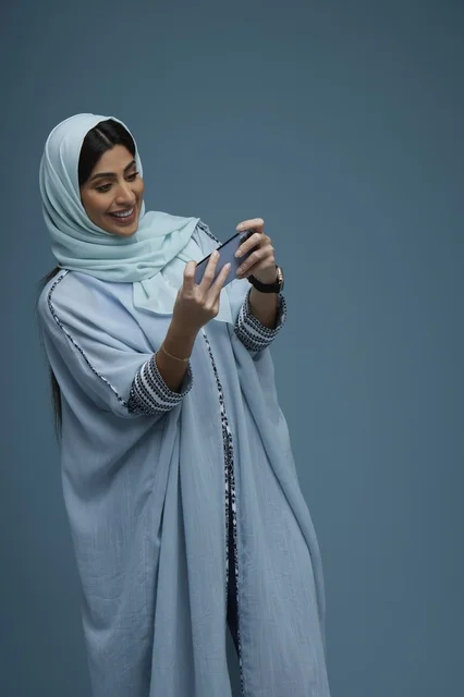 امرأة سعودية تستخدم الهاتف الذكي أمام خلفية زرقاء