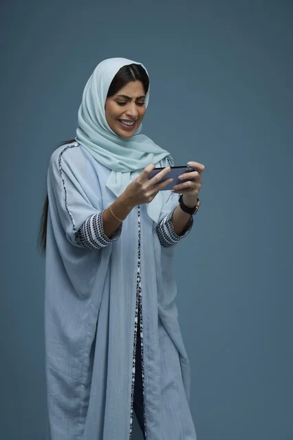 امرأة سعودية تستخدم الهاتف الذكي أمام خلفية زرقاء
