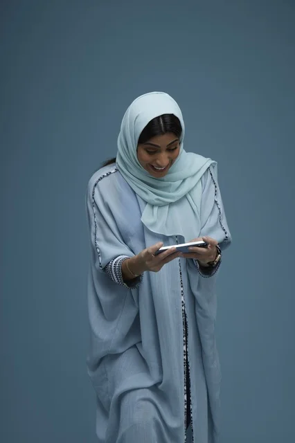 امرأة سعودية تستخدم الهاتف الذكي أمام خلفية زرقاء