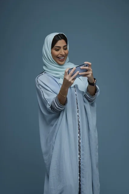 امرأة سعودية تستخدم الهاتف الذكي بخلفية زرقاء