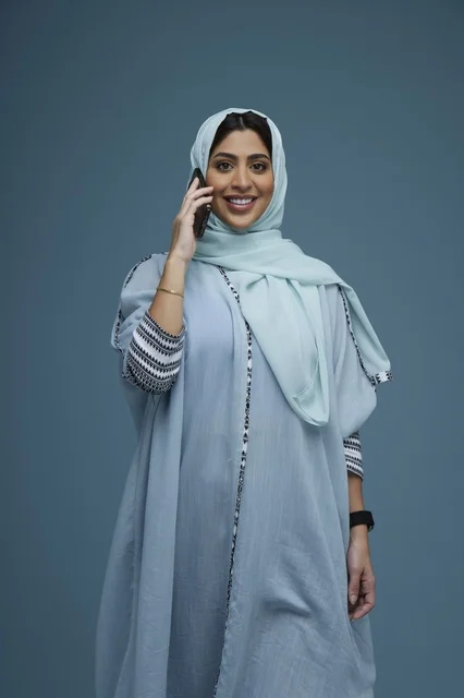 امرأة سعودية محجبة تتحدث بالهاتف الذكي خلفية زرقاء