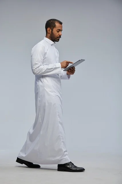 Saudi Man in White Thobe Walking with Tablet