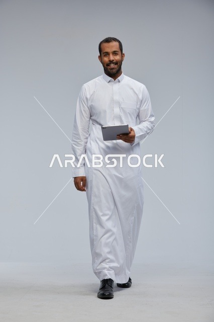 رجل سعودي بالثوب الأبيض يستخدم جهازاً لوحياً