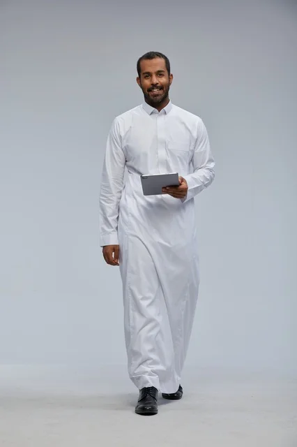 رجل سعودي بالثوب الأبيض يستخدم جهازاً لوحياً
