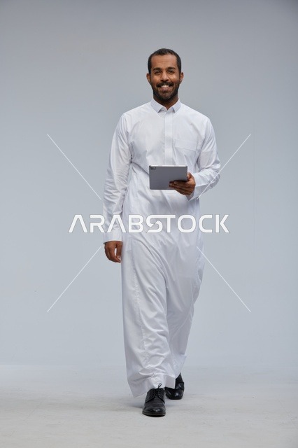 رجل سعودي بالثوب الأبيض يمسك جهاز لوحي