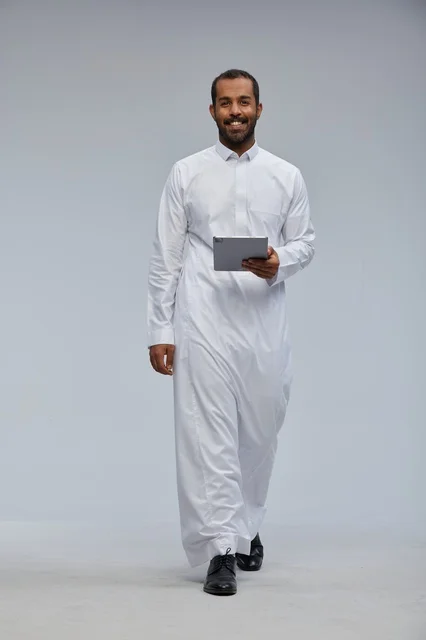 رجل سعودي بالثوب الأبيض يمسك جهاز لوحي