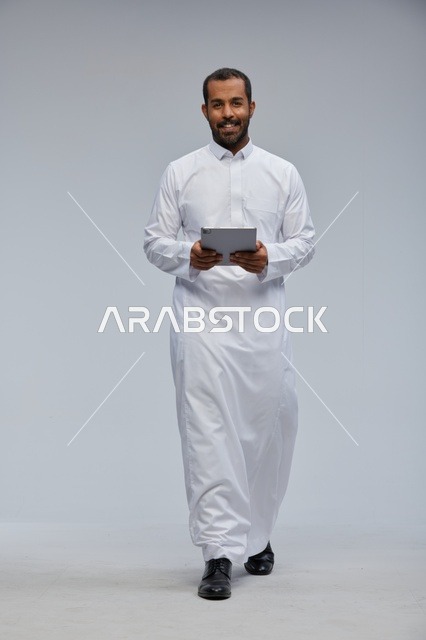 رجل سعودي بالثوب الأبيض يستخدم جهاز لوحي في الاستوديو