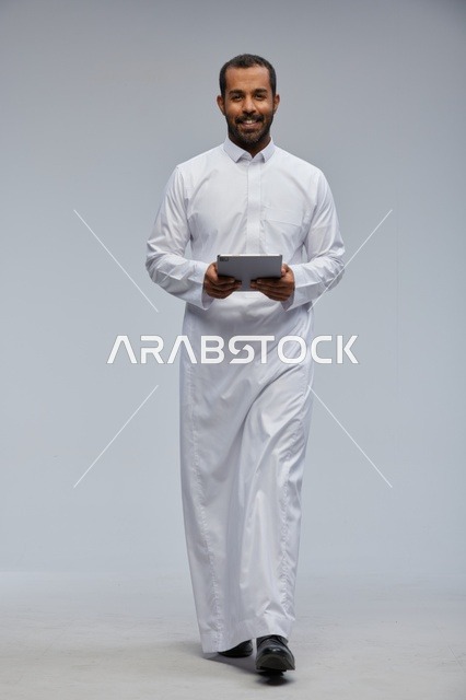 رجل سعودي بالثوب الأبيض يستخدم جهاز لوحي
