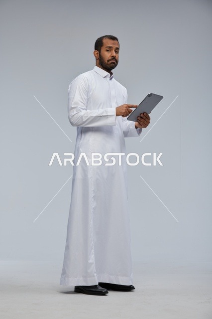رجل سعودي يرتدي الثوب الأبيض التقليدي يستخدم جهاز لوحي
