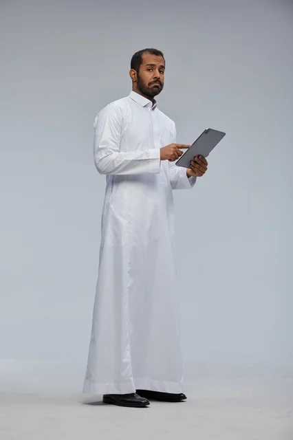 رجل سعودي يرتدي الثوب الأبيض التقليدي يستخدم جهاز لوحي