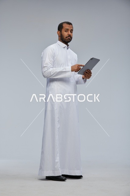 رجل سعودي بالثوب الأبيض يستخدم جهاز لوحي في الاستوديو