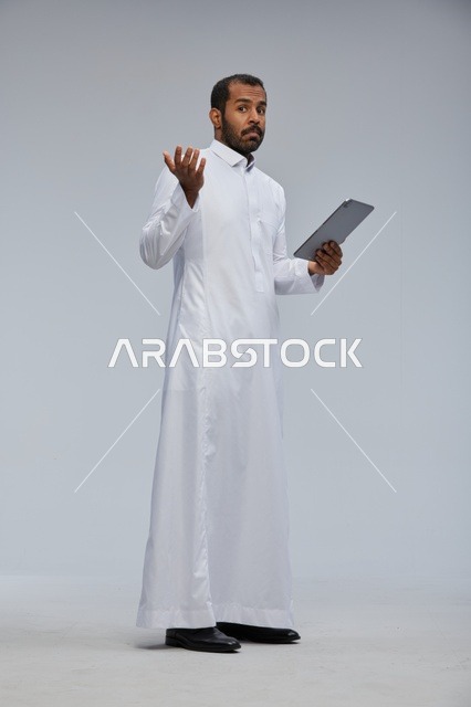 رجل سعودي بثوب أبيض يستخدم جهازًا لوحيًا