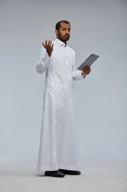رجل سعودي بالثوب الأبيض يستخدم جهازاً لوحياً في الاستوديو