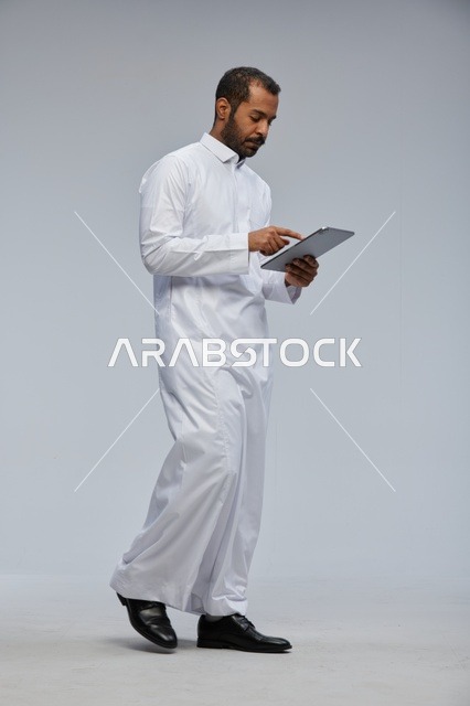 رجل سعودي بالثوب الأبيض يستخدم جهاز لوحي في الاستوديو