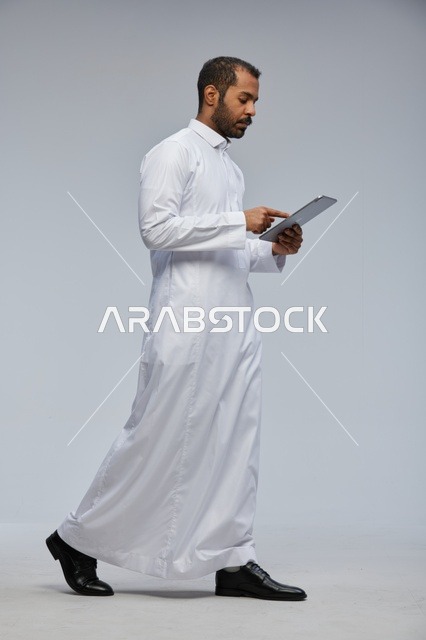 رجل سعودي يرتدي الثوب الأبيض ويستخدم جهازًا لوحيًا