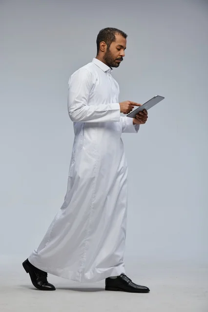 رجل سعودي يرتدي الثوب الأبيض ويستخدم جهازًا لوحيًا