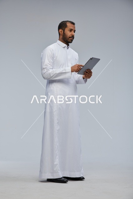 رجل سعودي بالثوب الأبيض يستخدم جهازاً لوحياً