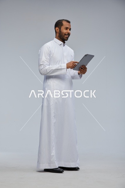 رجل سعودي بالثوب الأبيض يستخدم جهازًا لوحيًا في الاستوديو