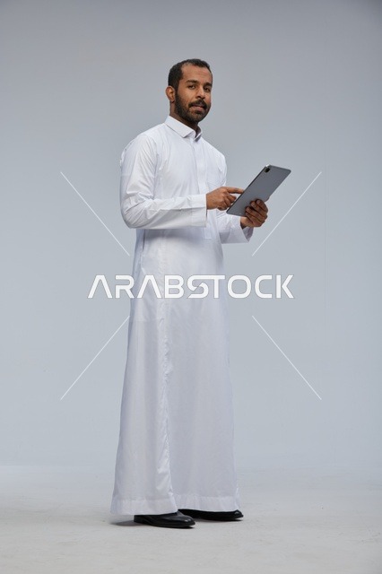 رجل سعودي بالثوب الأبيض يستخدم جهازاً لوحياً
