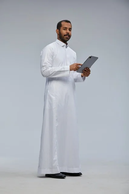 رجل سعودي بالثوب الأبيض يستخدم جهازاً لوحياً