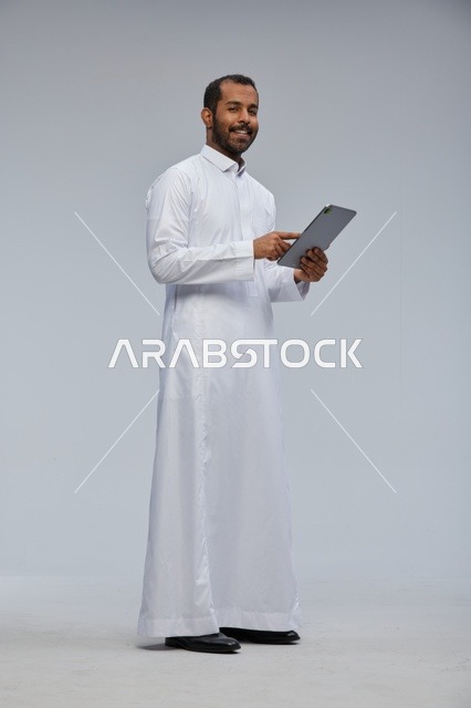 رجل سعودي بالثوب الأبيض يستخدم جهاز لوحي